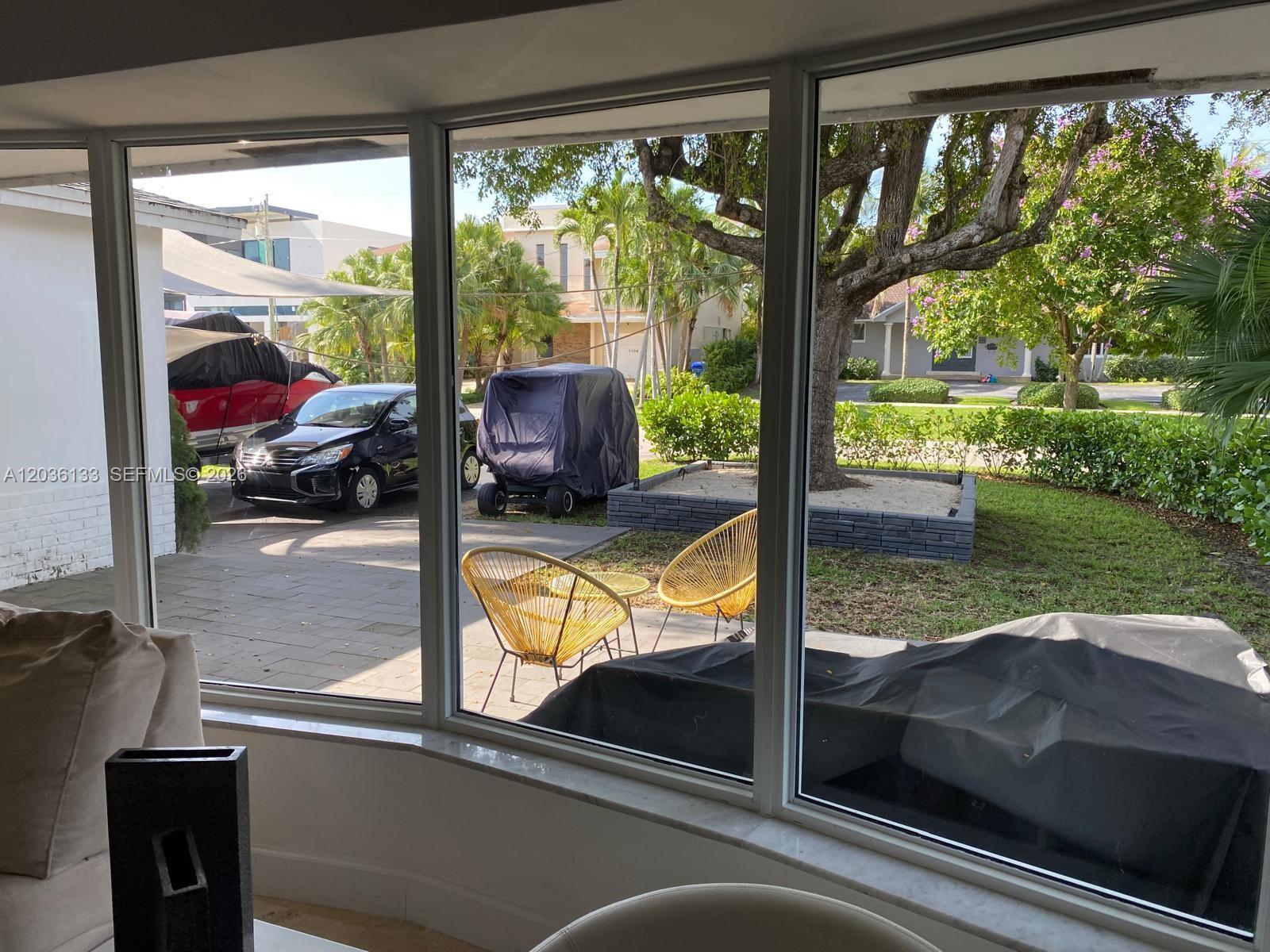A view through a large bay window looking out onto a driveway, patio, and yard — 1103 Washington St, Hollywood FL 33019, HOLLYWOOD, FL