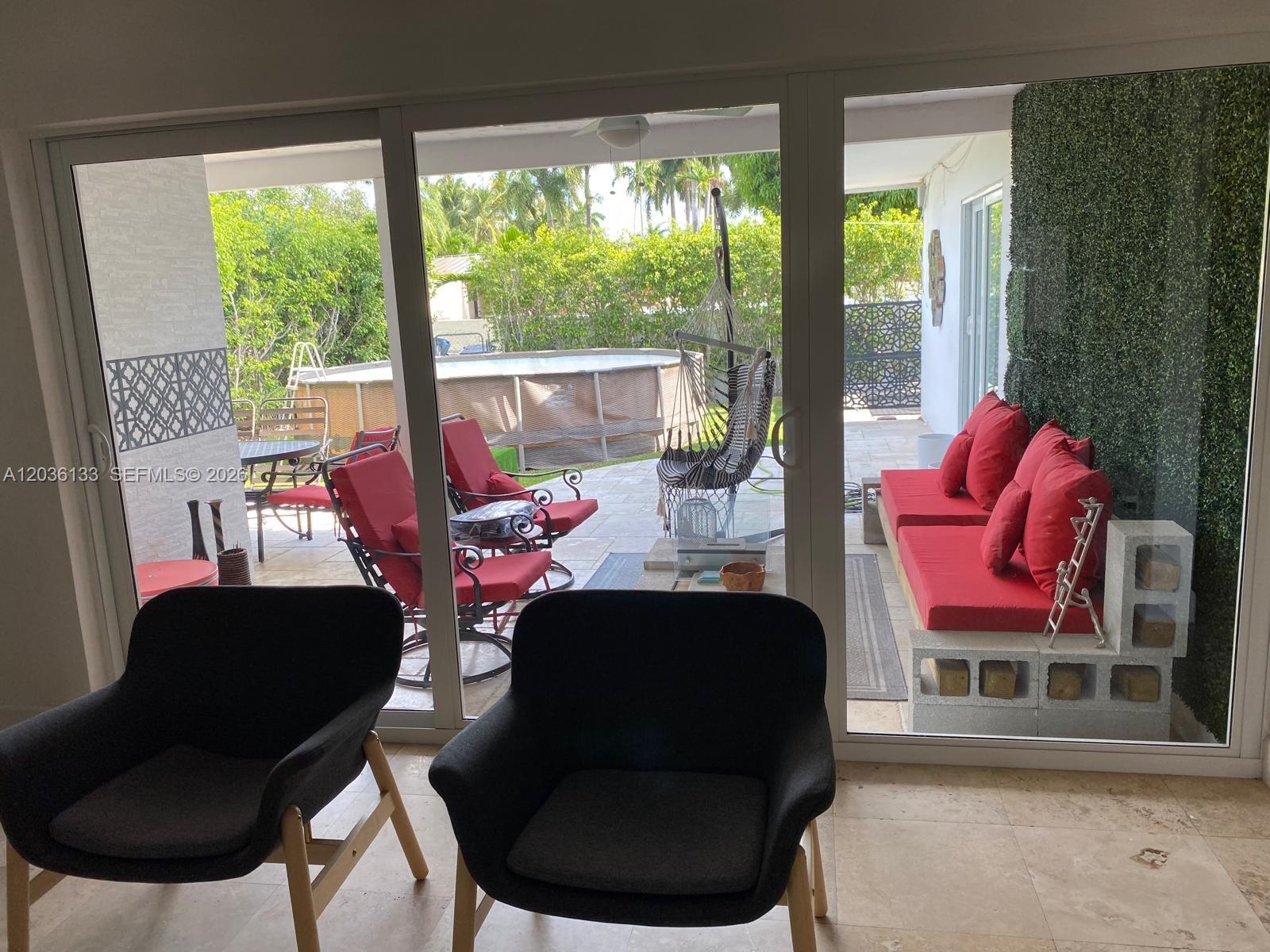 A view through sliding glass doors shows a patio with red seating and a pool — 1103 Washington St, Hollywood FL 33019, HOLLYWOOD, FL