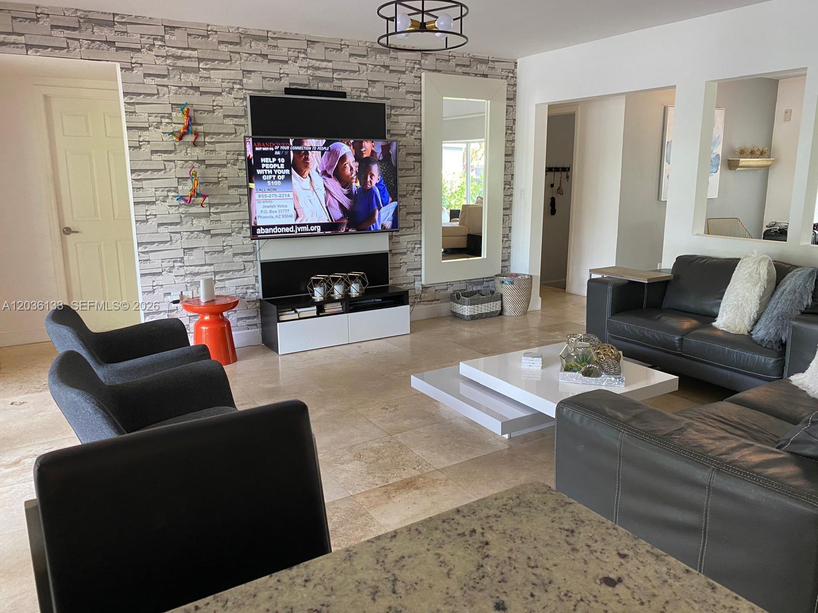 A living room features a stone-accented wall, a mounted television, and dark leather furniture — 1103 Washington St, Hollywood FL 33019, HOLLYWOOD, FL