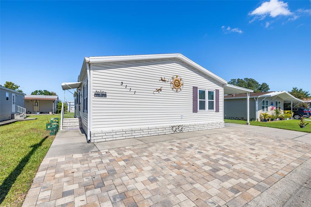 A light-colored manufactured home features a paved driveway, a carport, and a sun wall decoration — 3111 SHORT LEAF STREET, WESLEY CHAPEL, FL