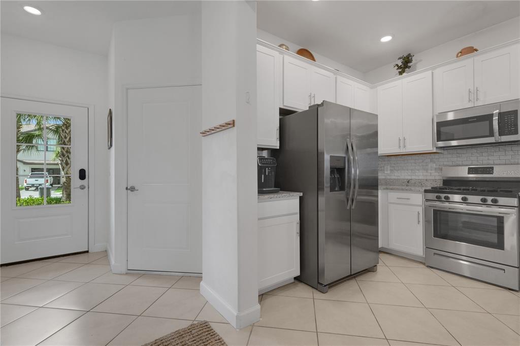 A kitchen features white cabinets, stainless steel appliances, a tiled backsplash, and a side door — 15227 SUNNY DAY DRIVE, BRADENTON, FL