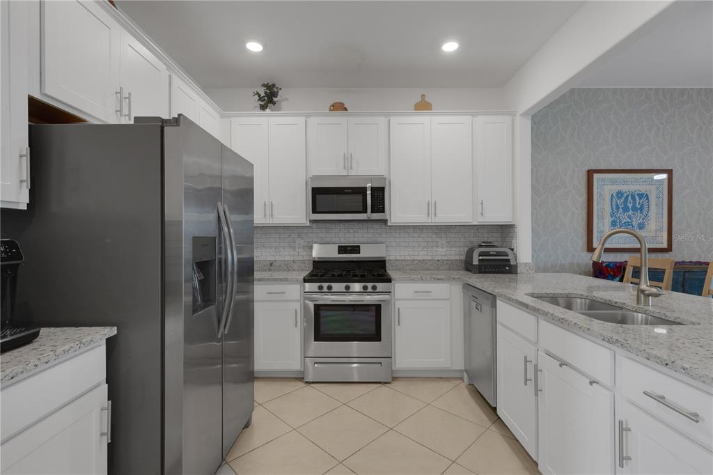 A kitchen features white cabinets, stainless steel appliances, granite countertops, and a tiled floor — 15227 SUNNY DAY DRIVE, BRADENTON, FL