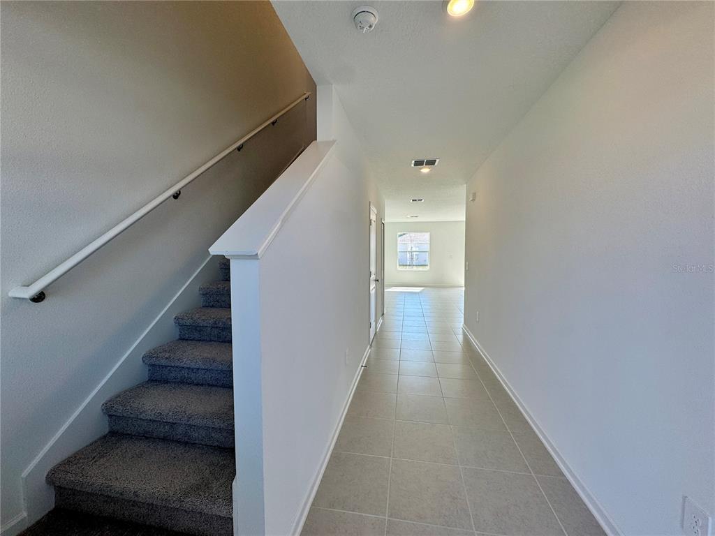 A hallway with tile flooring leads to a bright room, with carpeted stairs on the left — 405 KAYDEN COVE, WINTER HAVEN, FL