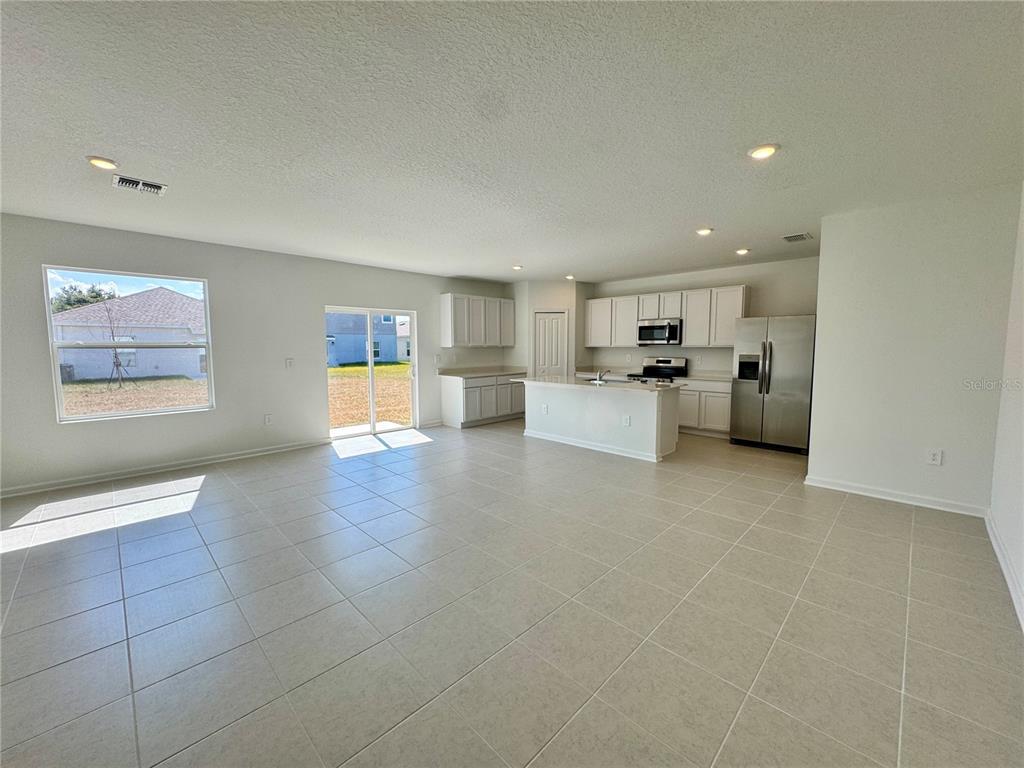 An open-concept kitchen and living area features light tile flooring, white cabinetry, and stainless appliances — 405 KAYDEN COVE, WINTER HAVEN, FL
