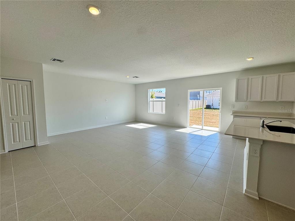 An open-concept living area features light tile flooring, white walls, and a sliding glass door — 405 KAYDEN COVE, WINTER HAVEN, FL