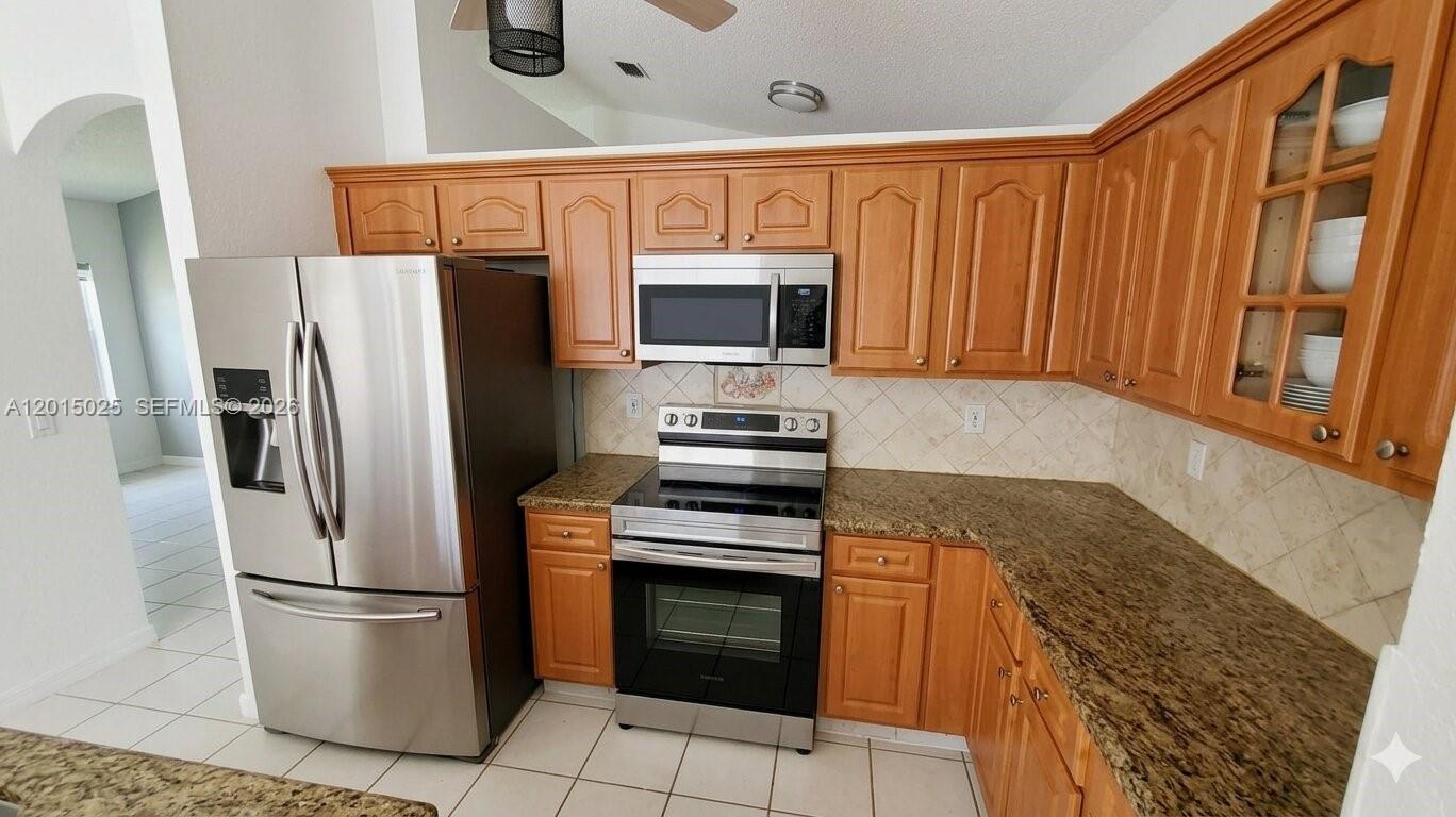 A kitchen features wood cabinets, granite countertops, stainless steel appliances, and a tile backsplash — 10273 SW 162nd Ct, Miami FL 33196, MIAMI, FL