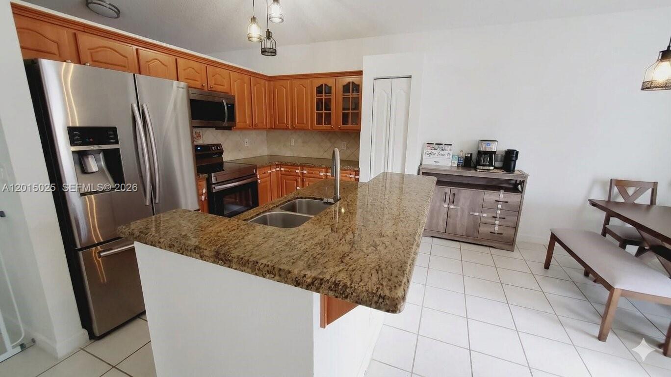 A kitchen features wood cabinets, granite countertops, stainless steel appliances, and a dining area — 10273 SW 162nd Ct, Miami FL 33196, MIAMI, FL