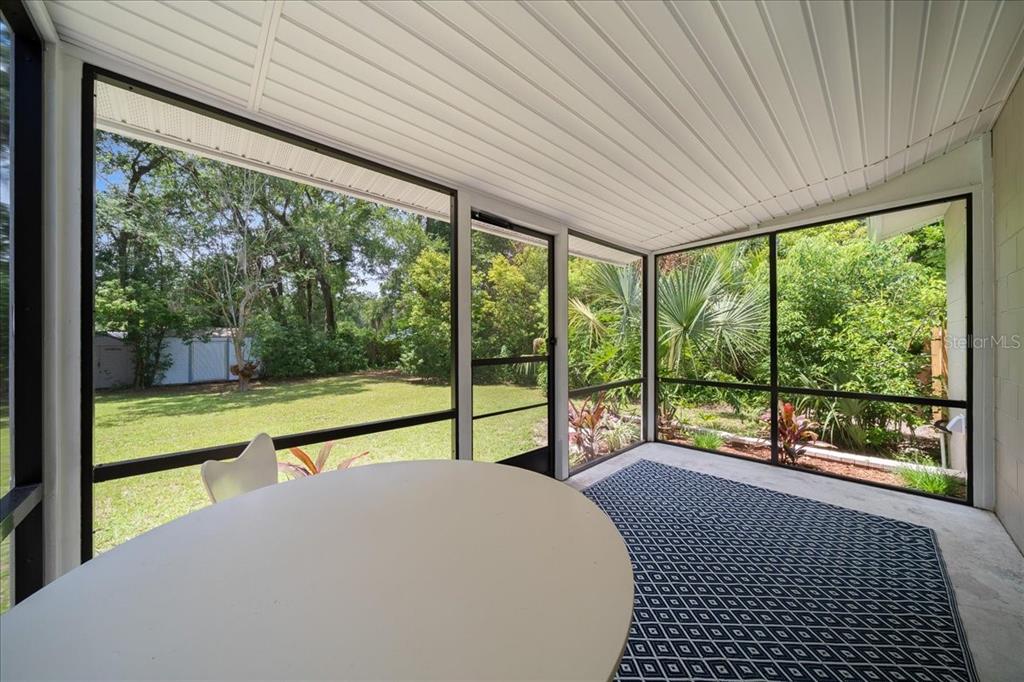 A screened-in porch features a white table, a patterned rug, and views of a backyard — 3164 SE 11TH STREET, OCALA, FL