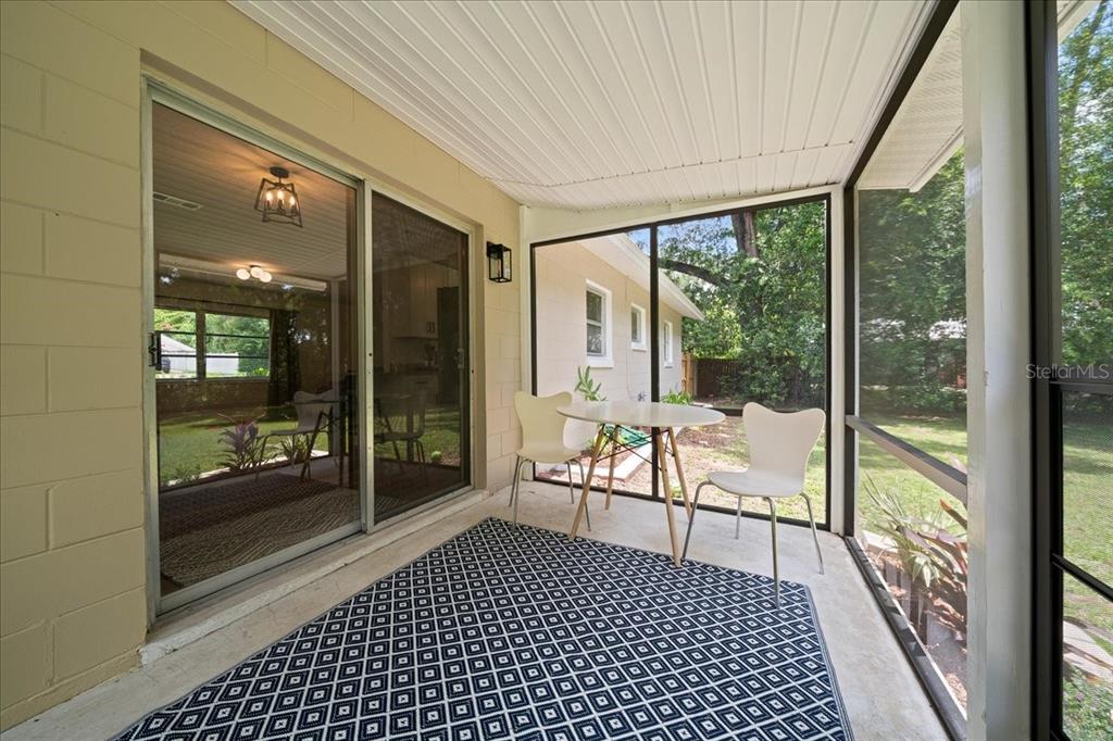 A screened-in porch features a patterned rug, a small table with two chairs, and sliding doors — 3164 SE 11TH STREET, OCALA, FL
