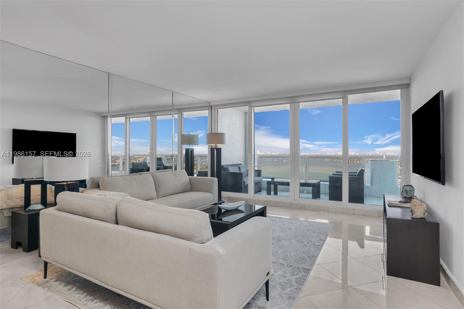 A living room features a light sofa, mirrored wall, tile flooring, and a balcony with water views — 1717 N Bayshore Dr # 3332, Miami FL 33132, MIAMI, FL