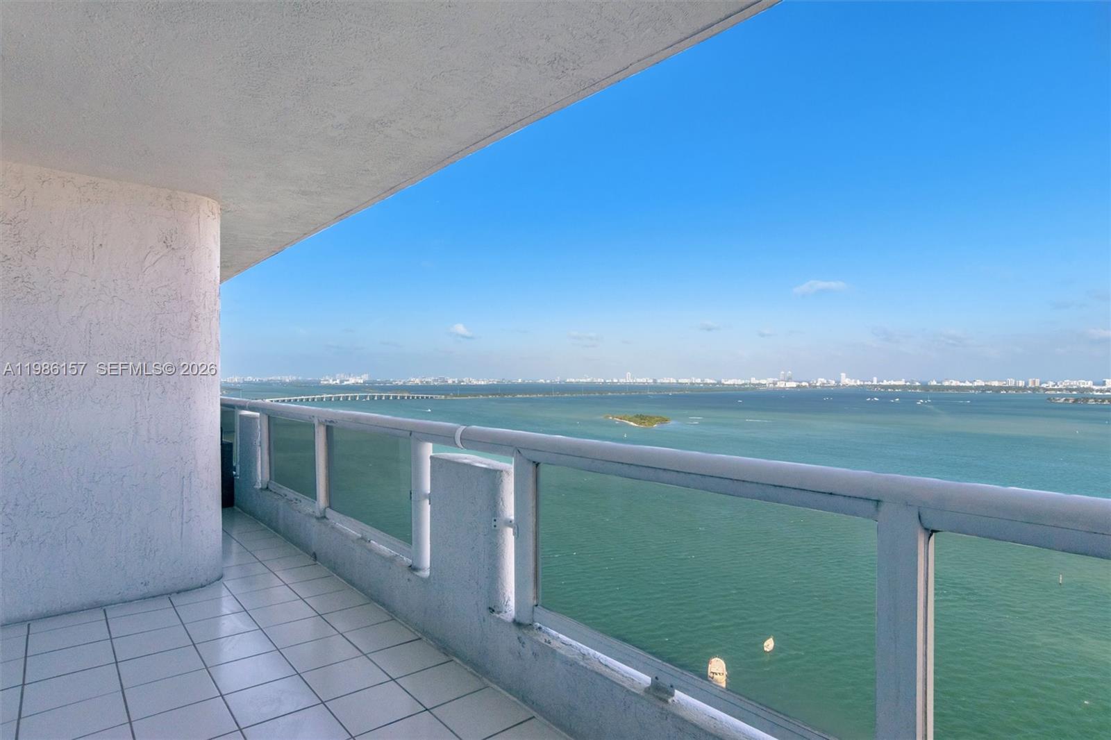A high-rise balcony with a tiled floor and glass railing overlooks a bay — 1717 N Bayshore Dr # 3332, Miami FL 33132, MIAMI, FL