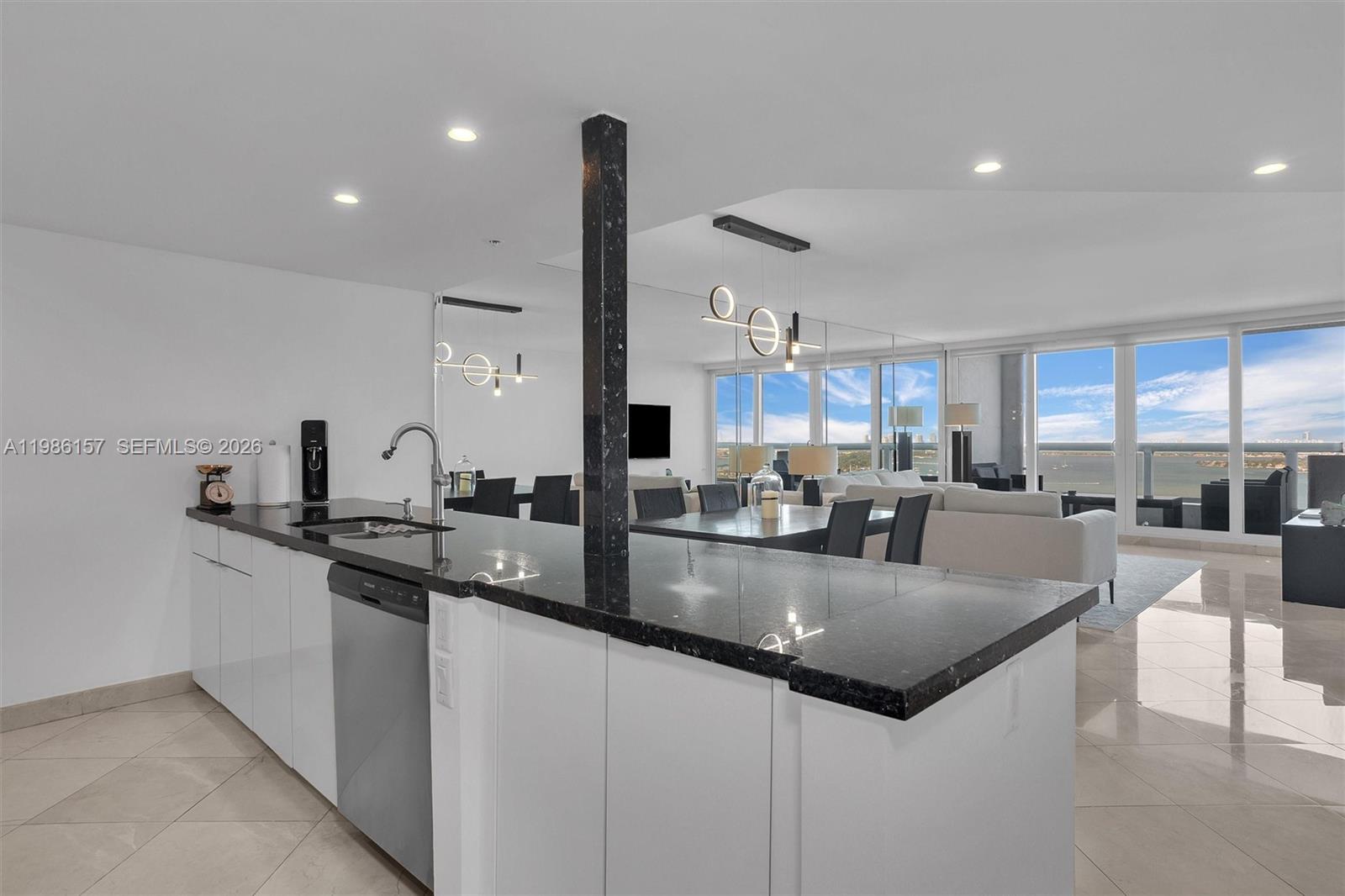 A modern kitchen with black granite countertops and white cabinets overlooks a bright living area — 1717 N Bayshore Dr # 3332, Miami FL 33132, MIAMI, FL