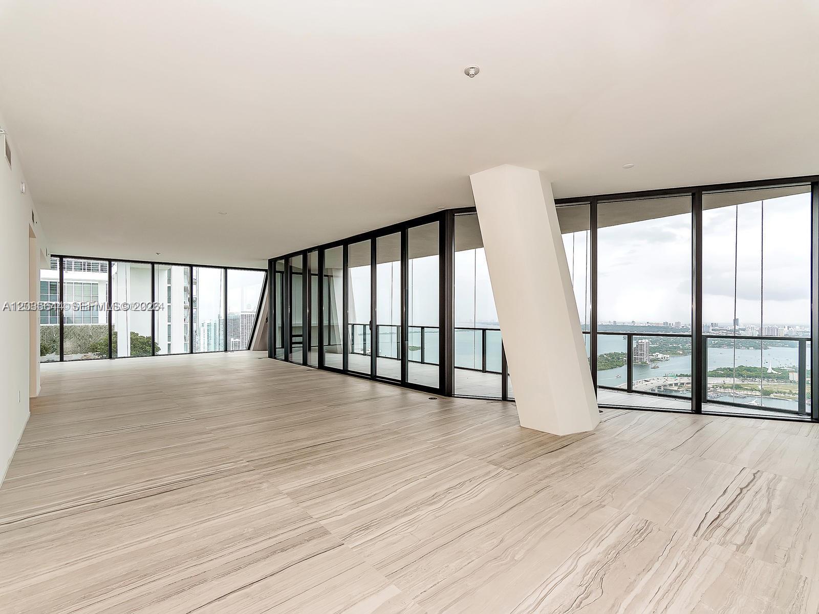An empty room features floor-to-ceiling windows, light wood-look tile flooring, and a slanted support column — 1000 Biscayne Blvd # 4802, Miami FL 33132, MIAMI, FL