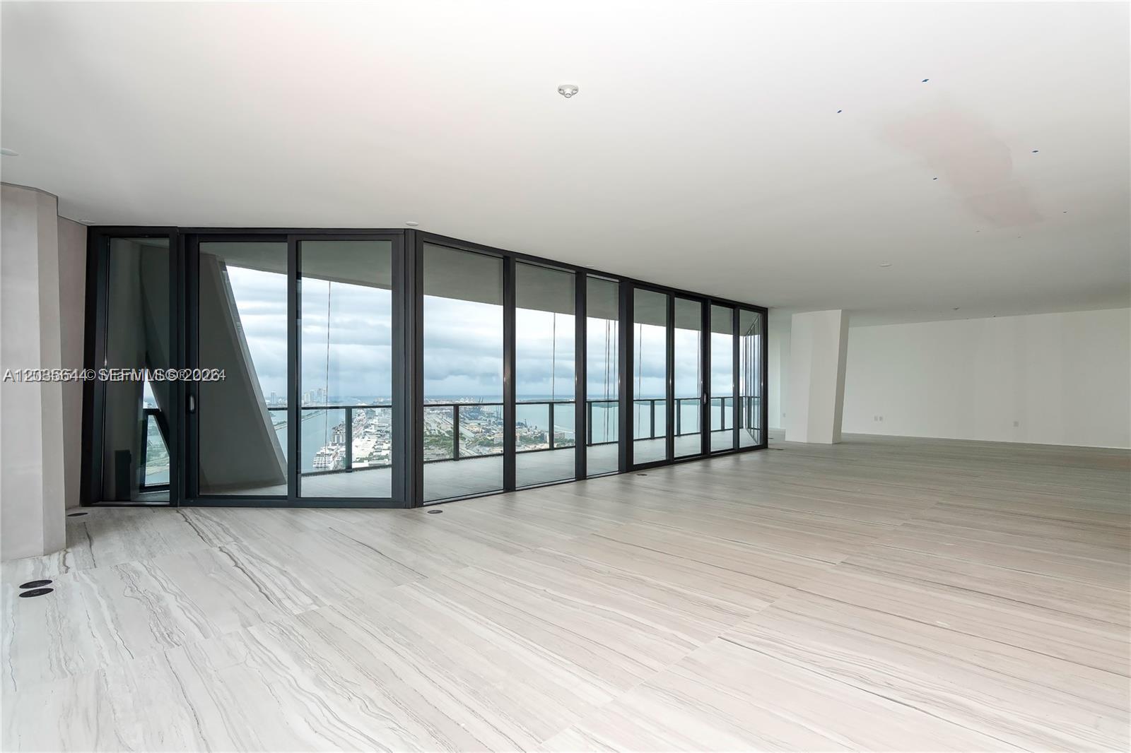 An empty room features large floor-to-ceiling windows, light-colored stone flooring, and a balcony view — 1000 Biscayne Blvd # 4802, Miami FL 33132, MIAMI, FL