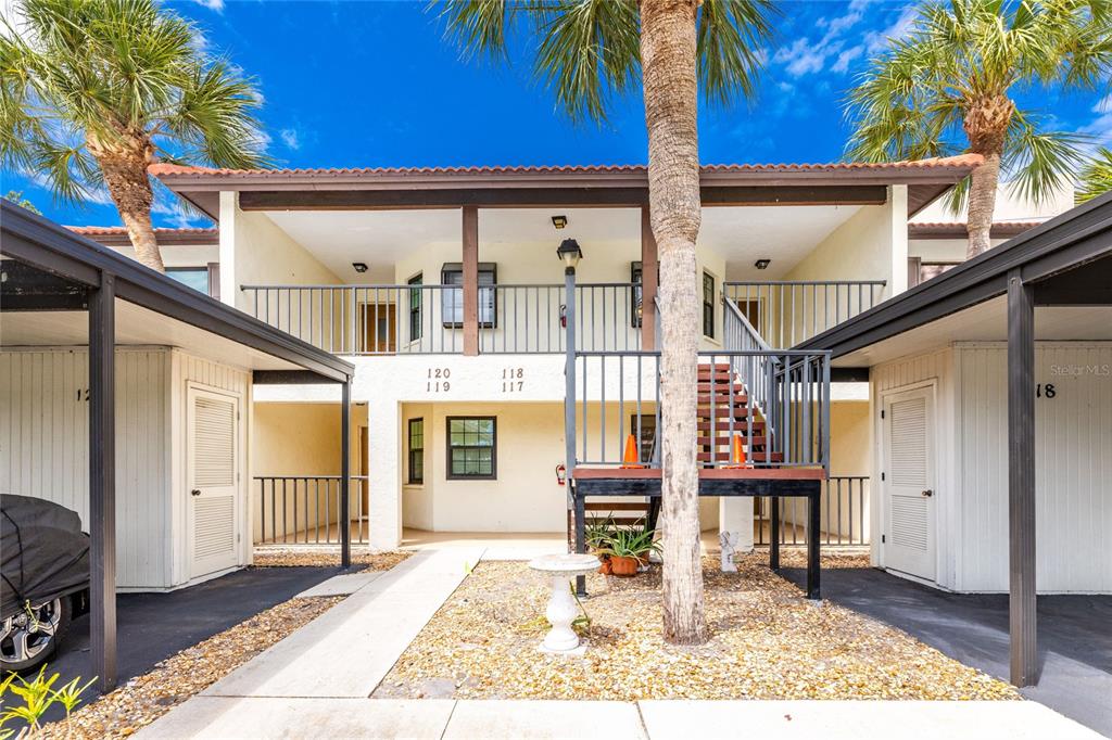 A two-story apartment building exterior features covered parking, a central staircase, and palm trees — 118 PINE HOLLOW DRIVE UNIT 118, ENGLEWOOD, FL