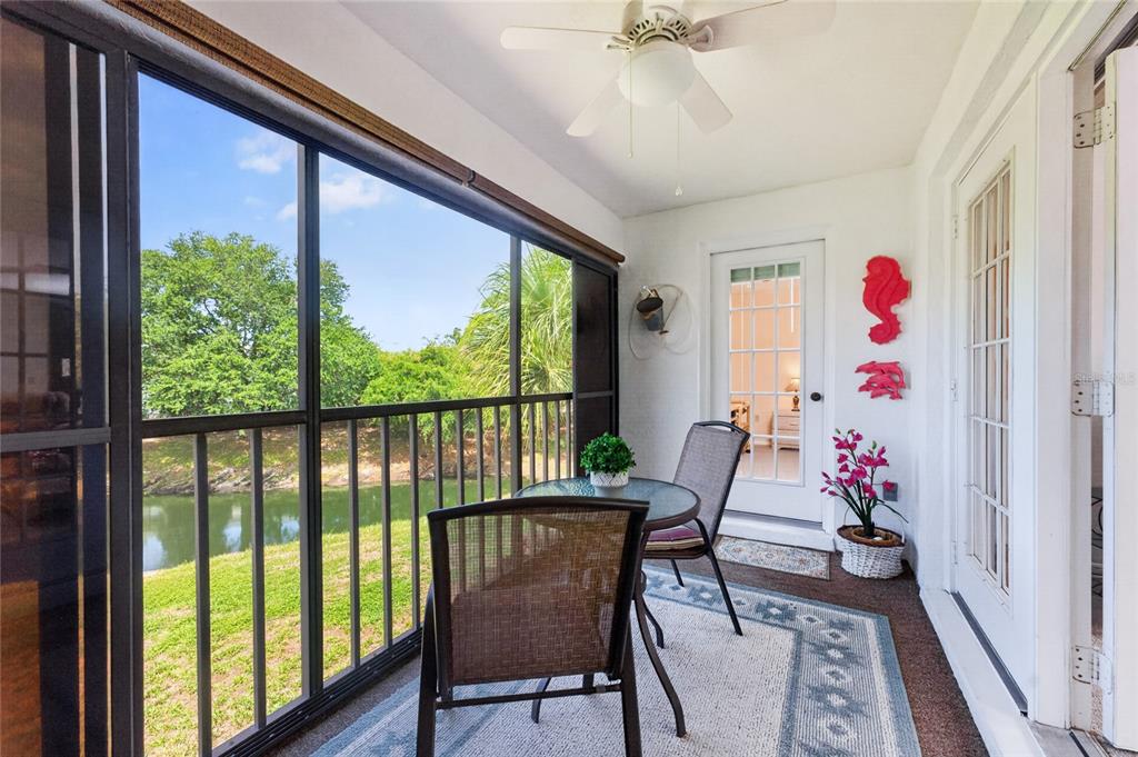 A screened-in porch features a small table, two chairs, and a view of a canal — 118 PINE HOLLOW DRIVE UNIT 118, ENGLEWOOD, FL