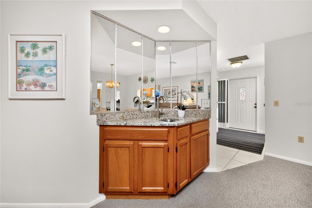 A wet bar with a granite countertop and mirrored backsplash sits in a carpeted room — 118 PINE HOLLOW DRIVE UNIT 118, ENGLEWOOD, FL