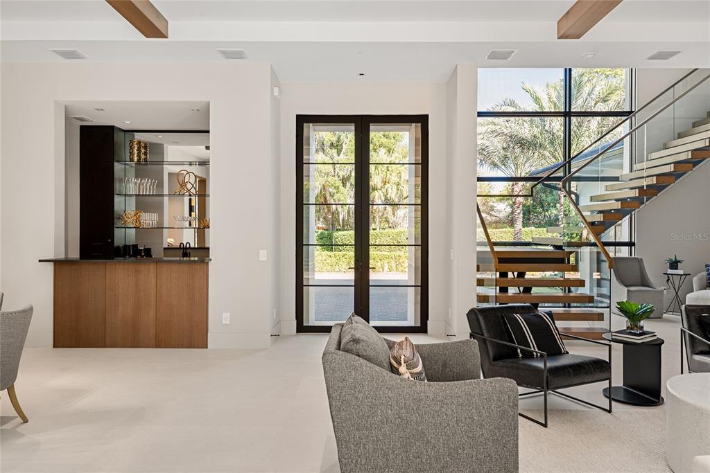 A modern living area features a wet bar, glass-paned doors, and a floating wooden staircase — 550 PALMER AVENUE, WINTER PARK, FL