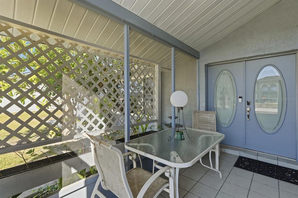 A covered patio features a glass-top table, chairs, lattice privacy screens, and double entry doors — 934 WILMINGTON DRIVE, DELTONA, FL