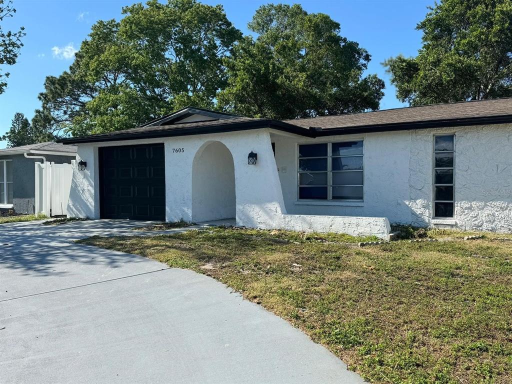 A white single-story house with a black garage door and a covered arched entryway — 7605 EMBASSY BOULEVARD, PORT RICHEY, FL