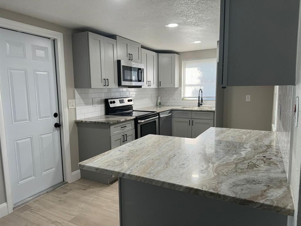 A kitchen features gray cabinets, granite countertops, a white subway tile backsplash, and stainless appliances — 7605 EMBASSY BOULEVARD, PORT RICHEY, FL