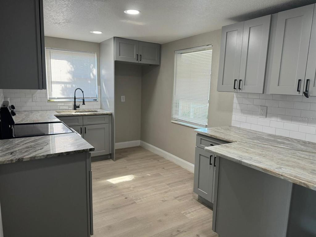 A kitchen with gray cabinets, light-colored countertops, white subway tile backsplash, and wood-look flooring — 7605 EMBASSY BOULEVARD, PORT RICHEY, FL