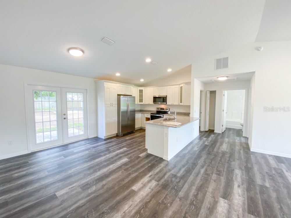 A kitchen with white cabinets, stainless steel appliances, and an island opens to a living area — 30 JUNIPER PASS LANE, OCALA, FL