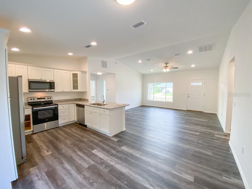 A kitchen with white cabinets and stainless steel appliances opens into a large living area — 30 JUNIPER PASS LANE, OCALA, FL