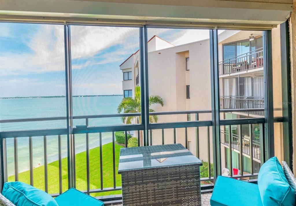 A screened-in balcony features a small table and two chairs overlooking a bay and buildings — 5541 PUERTA DEL SOL BOULEVARD S UNIT 316, ST PETERSBURG, FL
