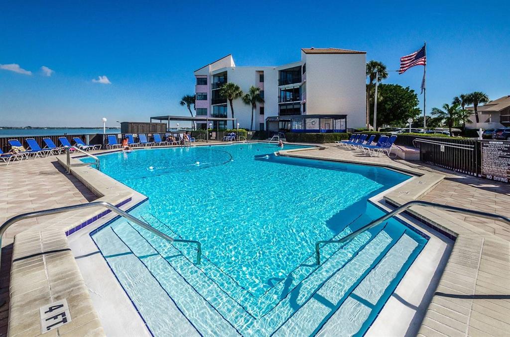 A swimming pool with steps and a handrail sits in front of a multi-story building — 5541 PUERTA DEL SOL BOULEVARD S UNIT 316, ST PETERSBURG, FL