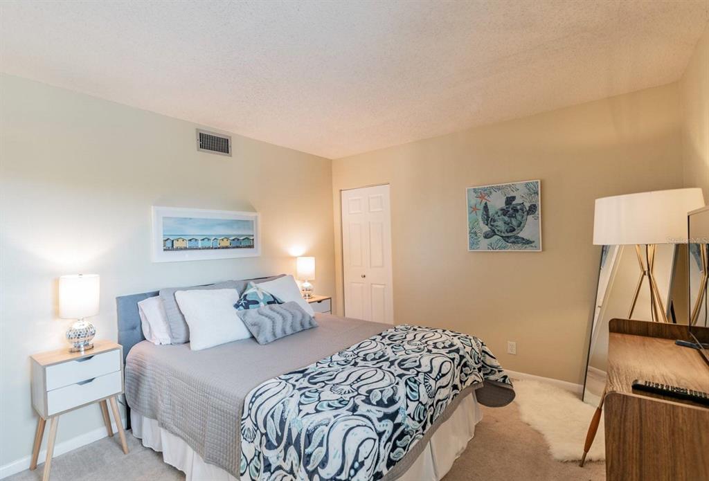A bedroom features a bed with patterned bedding, two nightstands, and a turtle wall art piece — 5541 PUERTA DEL SOL BOULEVARD S UNIT 316, ST PETERSBURG, FL