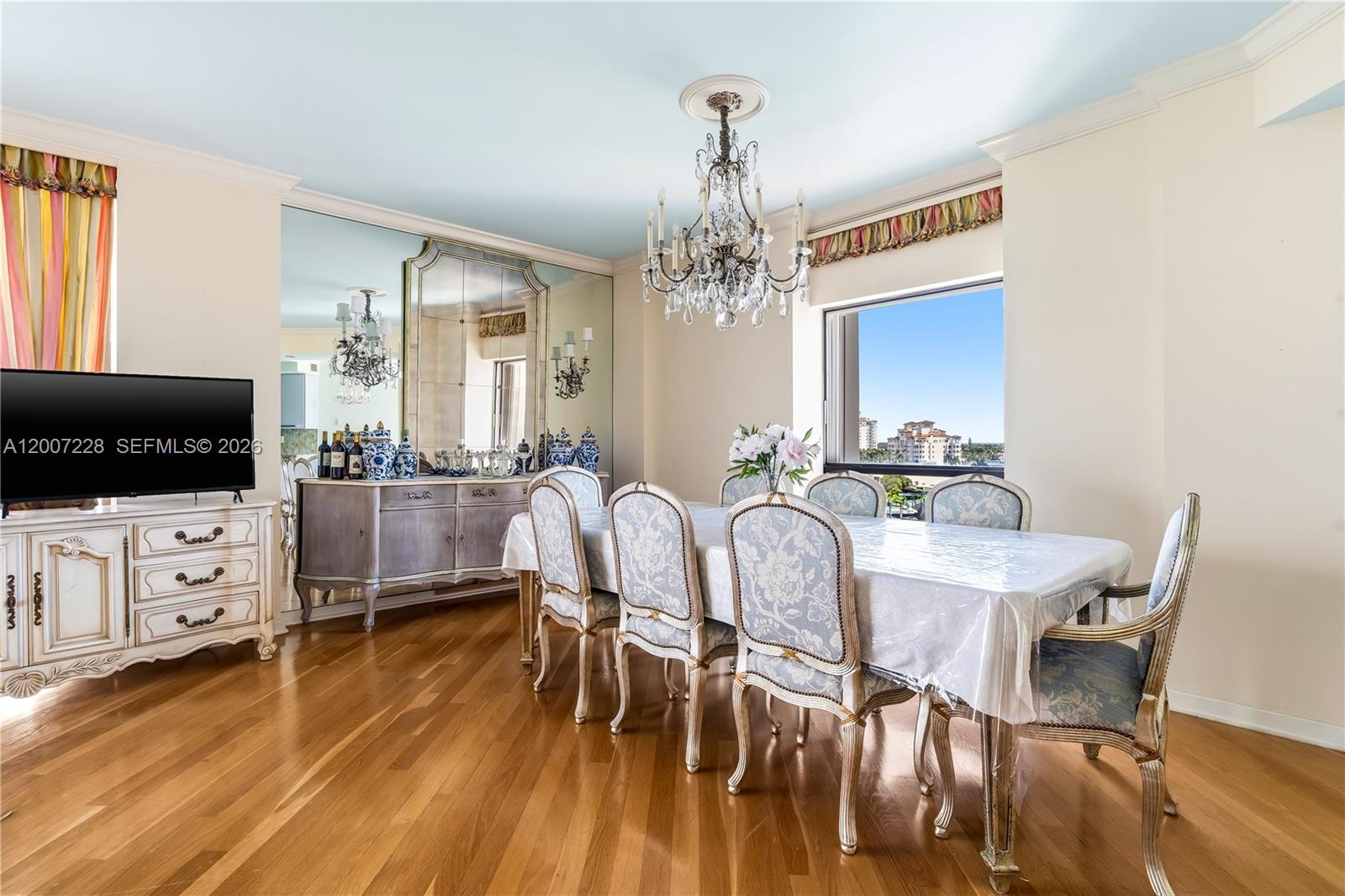 A dining room features a crystal chandelier, floral upholstered chairs, and a mirrored wall — AVENTURA, FL