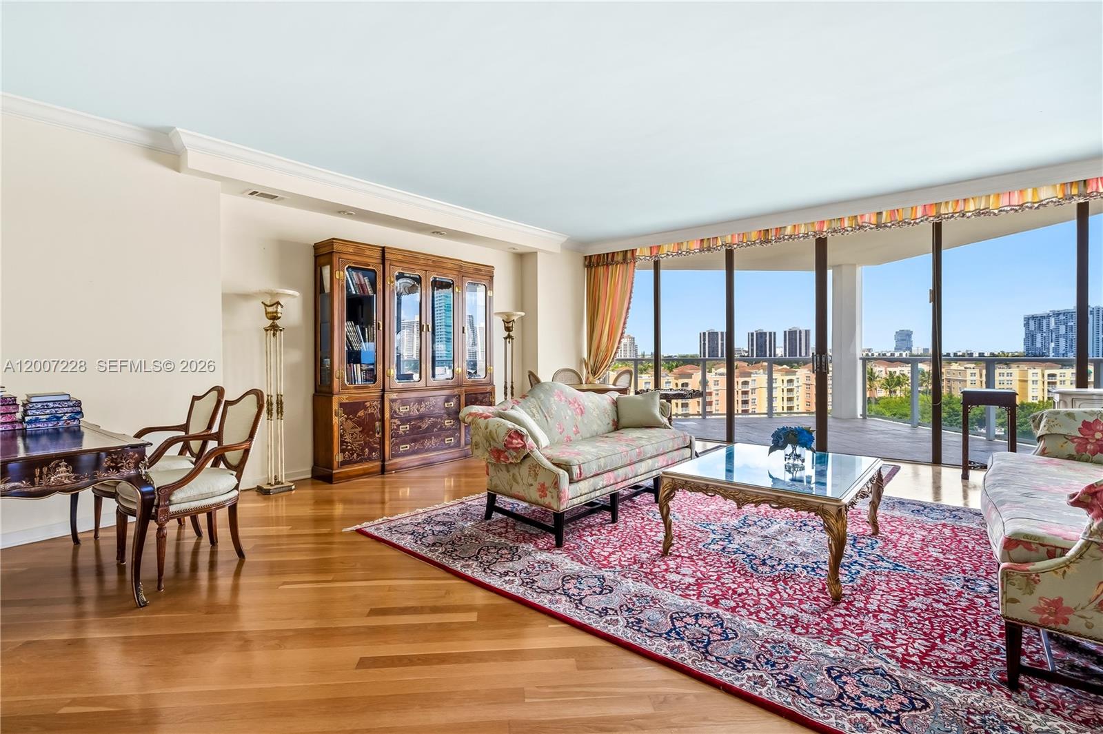 A living room features floral sofas, a red area rug, wood floors, and floor-to-ceiling windows — AVENTURA, FL