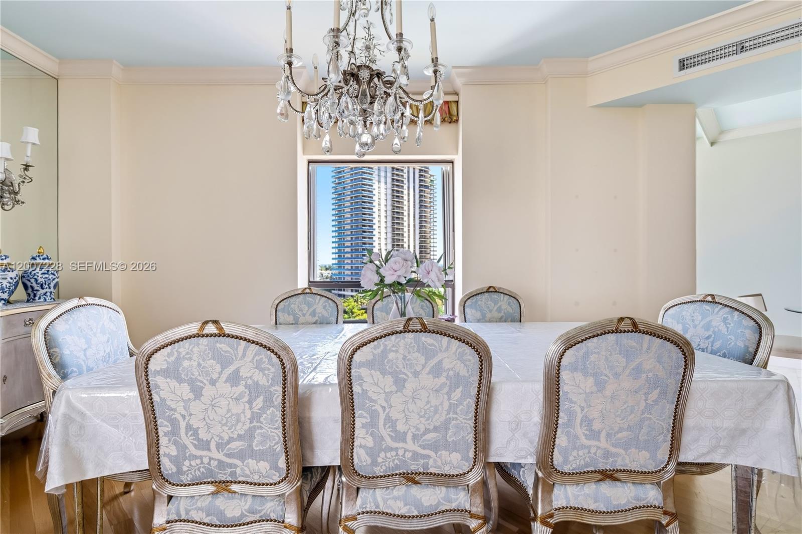 A formal dining room features a crystal chandelier, floral upholstered chairs, and a city view — AVENTURA, FL