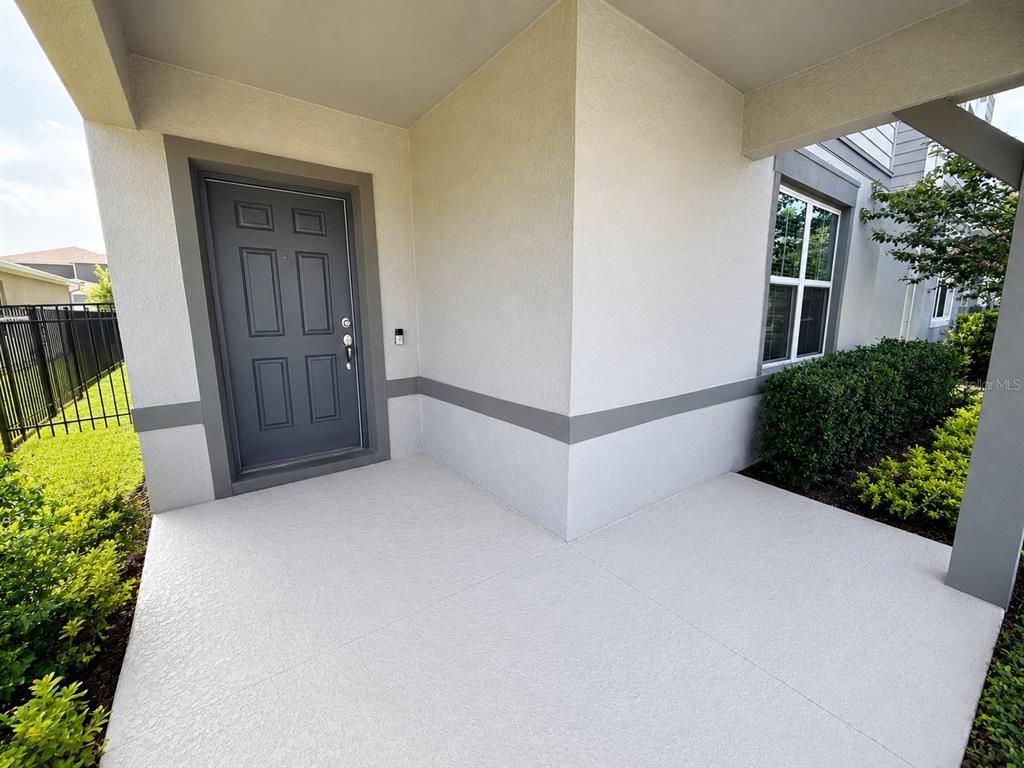 A covered concrete entryway features a gray front door and a window beside a hedge — 4083 FEATHER TREE DRIVE, APOPKA, FL