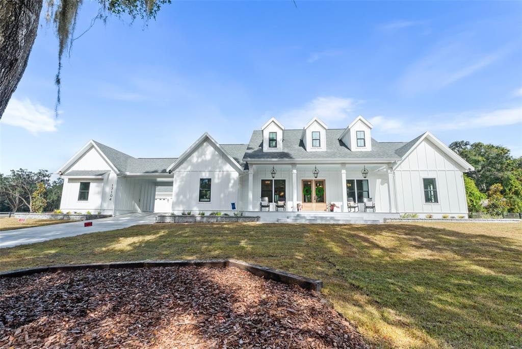 A white farmhouse-style home features a covered porch, three dormer windows, and a side garage — 17104 SW 11TH COURT, NEWBERRY, FL