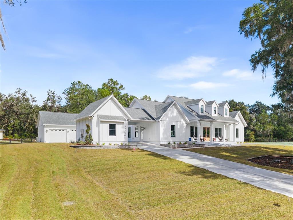 A white farmhouse with a detached garage and a long concrete driveway under a blue sky — 17104 SW 11TH COURT, NEWBERRY, FL