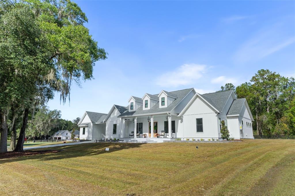A white farmhouse with a covered front porch and three dormers sits on a lawn — 17104 SW 11TH COURT, NEWBERRY, FL