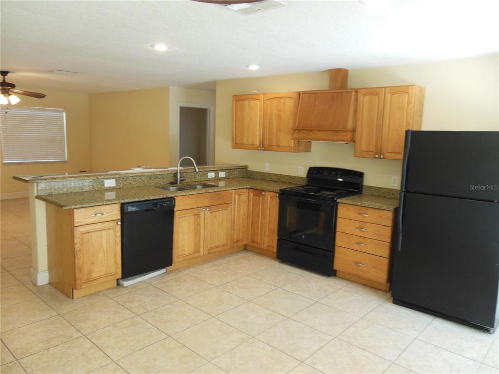 A kitchen features light wood cabinets, granite countertops, black appliances, and beige tile flooring — 213 BUTTONWOOD AVENUE, WINTER SPRINGS, FL
