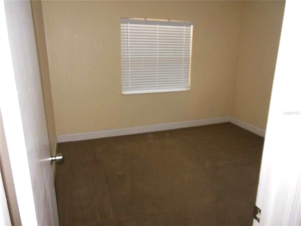 An empty bedroom features beige walls, brown carpeting, and a single window with white blinds — 213 BUTTONWOOD AVENUE, WINTER SPRINGS, FL