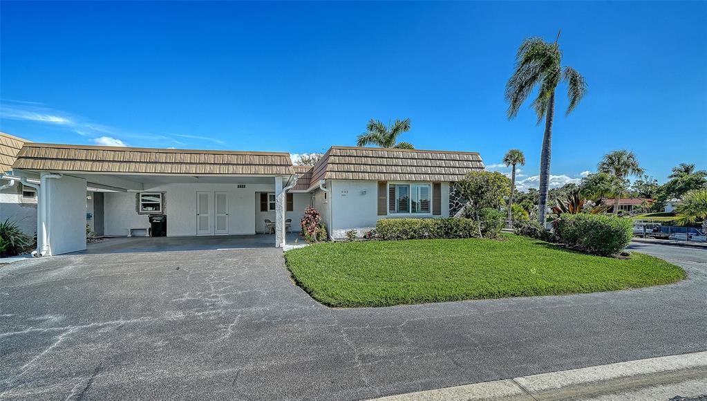 A single-story house with a carport, a manicured lawn, and palm trees under a blue sky — 2657 RIVERBLUFF PARKWAY UNIT V122, SARASOTA, FL