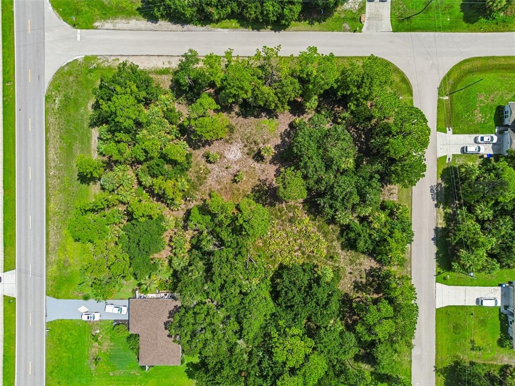An aerial view shows a wooded, undeveloped residential lot situated between two paved roads — 13 S CHAMBERLAIN BOULEVARD, NORTH PORT, FL