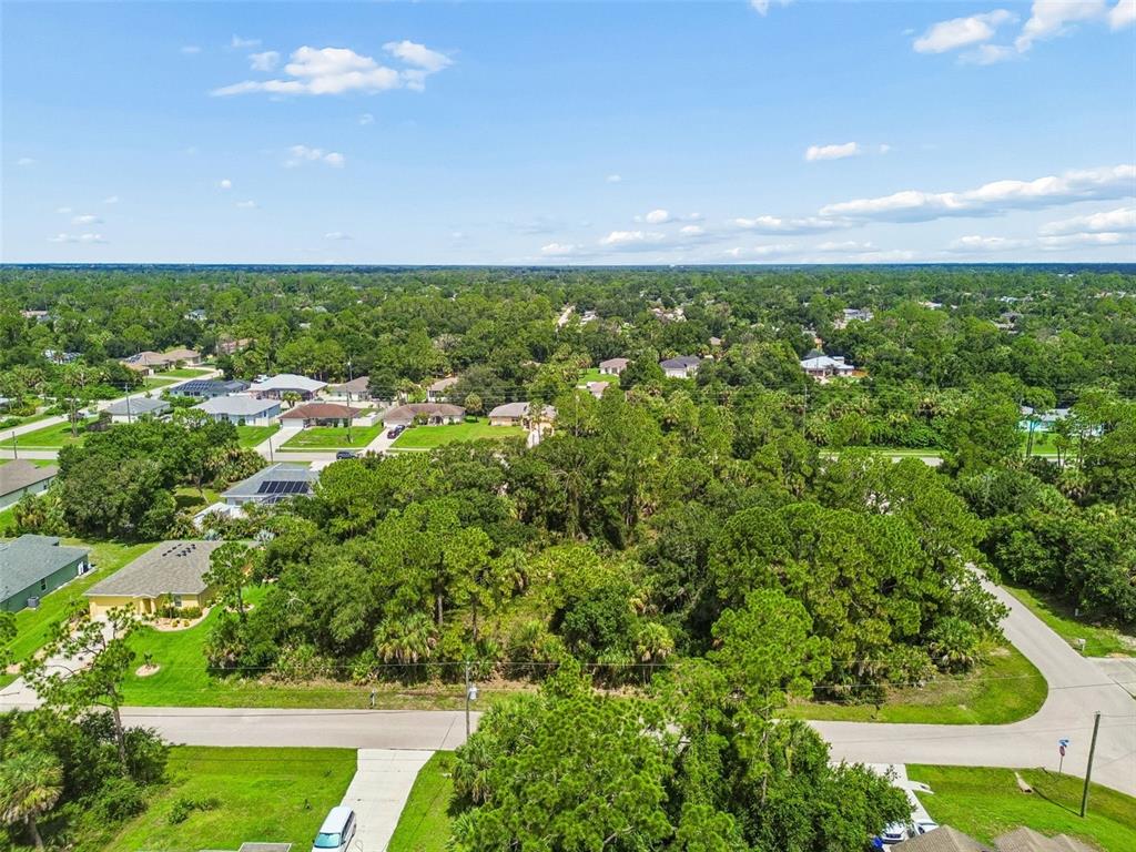 An aerial view shows a vacant, wooded residential lot surrounded by houses and streets — 13 S CHAMBERLAIN BOULEVARD, NORTH PORT, FL