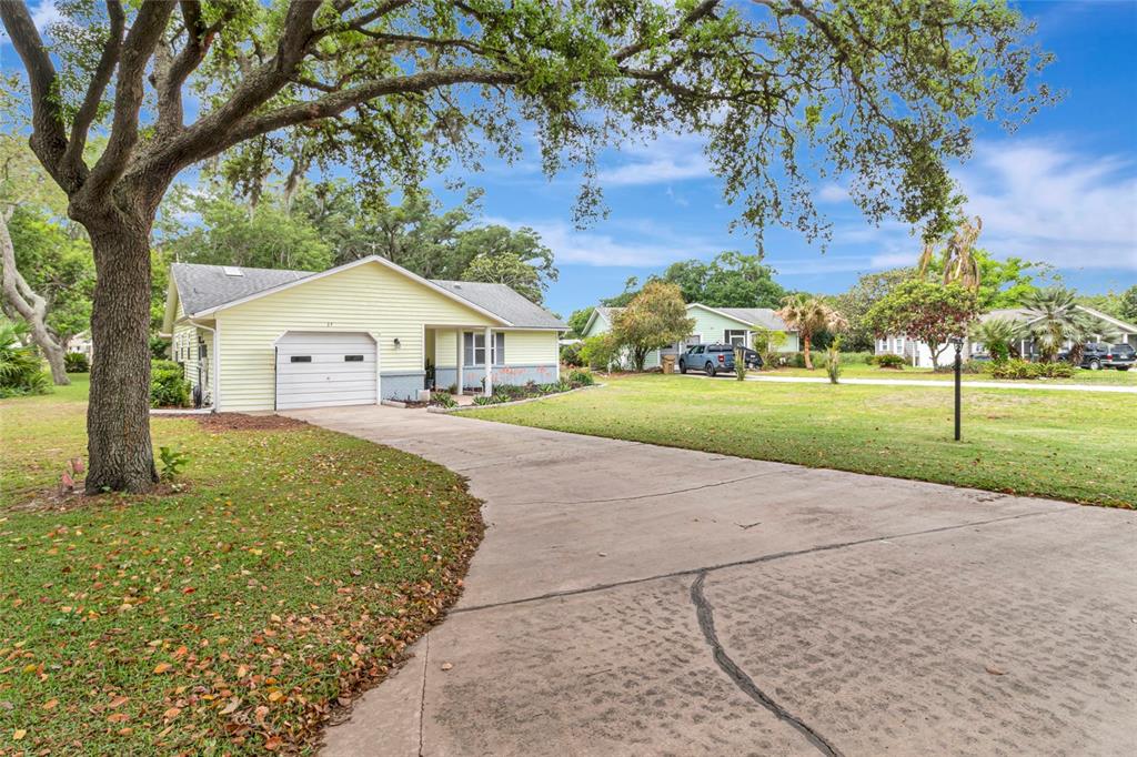 A light yellow single-story house with a garage and a concrete driveway under large trees — 27 GORDON COURT, LEESBURG, FL