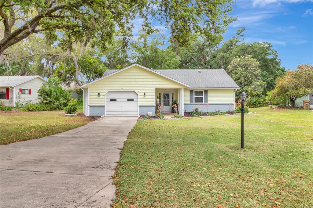 A single-story house with yellow siding, a gray roof, and a concrete driveway — 27 GORDON COURT, LEESBURG, FL