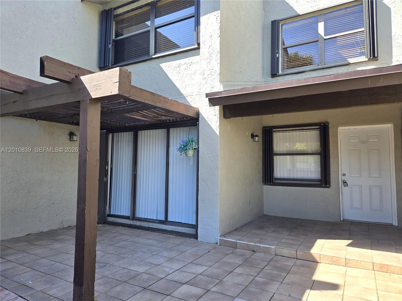 A patio with a wooden pergola, tiled flooring, sliding glass doors, and a front entrance — 10020 NW 9th St Cir # 102, Miami FL 33172, MIAMI, FL