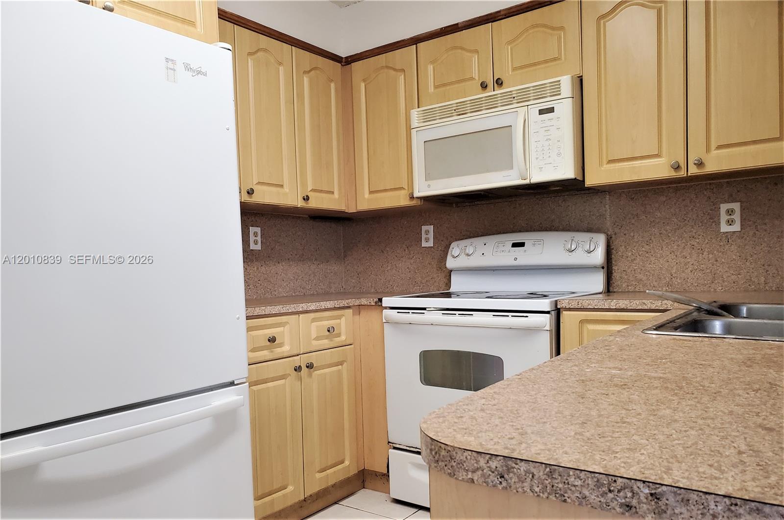 A kitchen features light wood cabinets, white appliances, and a speckled laminate countertop — 10020 NW 9th St Cir # 102, Miami FL 33172, MIAMI, FL