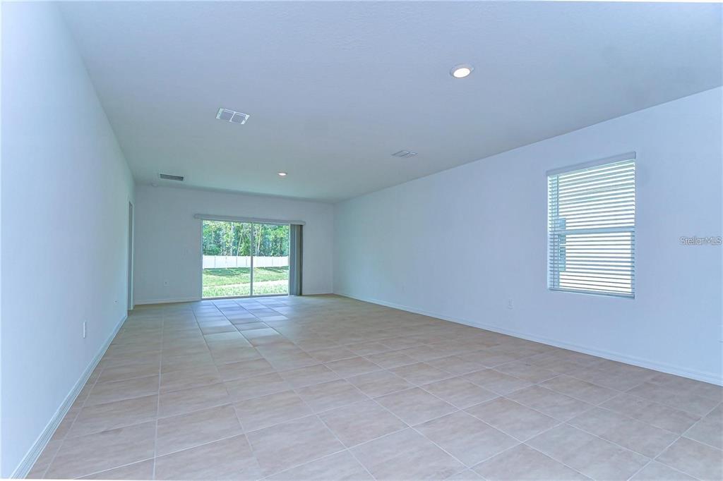 A spacious, empty living room features light-colored tile flooring, white walls, and a sliding glass door — 13341 TROPICAL BREEZE WAY, HUDSON, FL