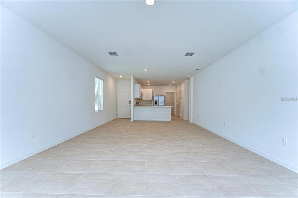 An open-concept living area features light-colored tile flooring, white walls, and a kitchen in the background — 13341 TROPICAL BREEZE WAY, HUDSON, FL