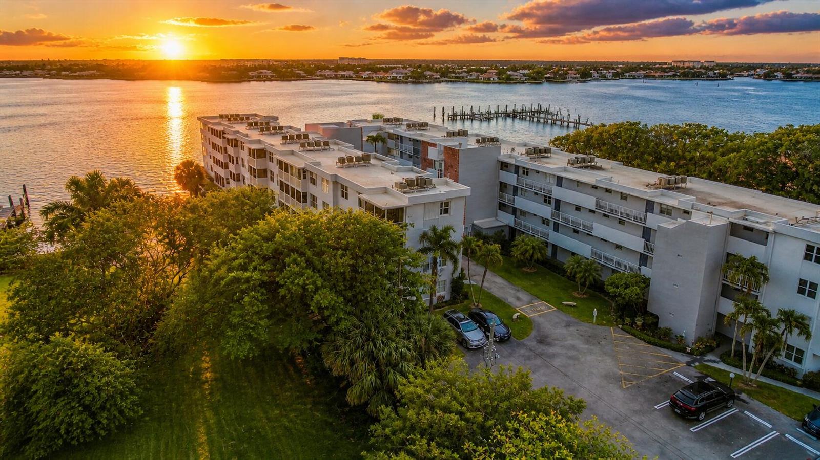 An aerial view of a multi-story apartment complex situated along a waterfront at sunset — 1820 New Palm Way # 308, Boynton Beach FL 33435, BOYNTON BEACH, FL
